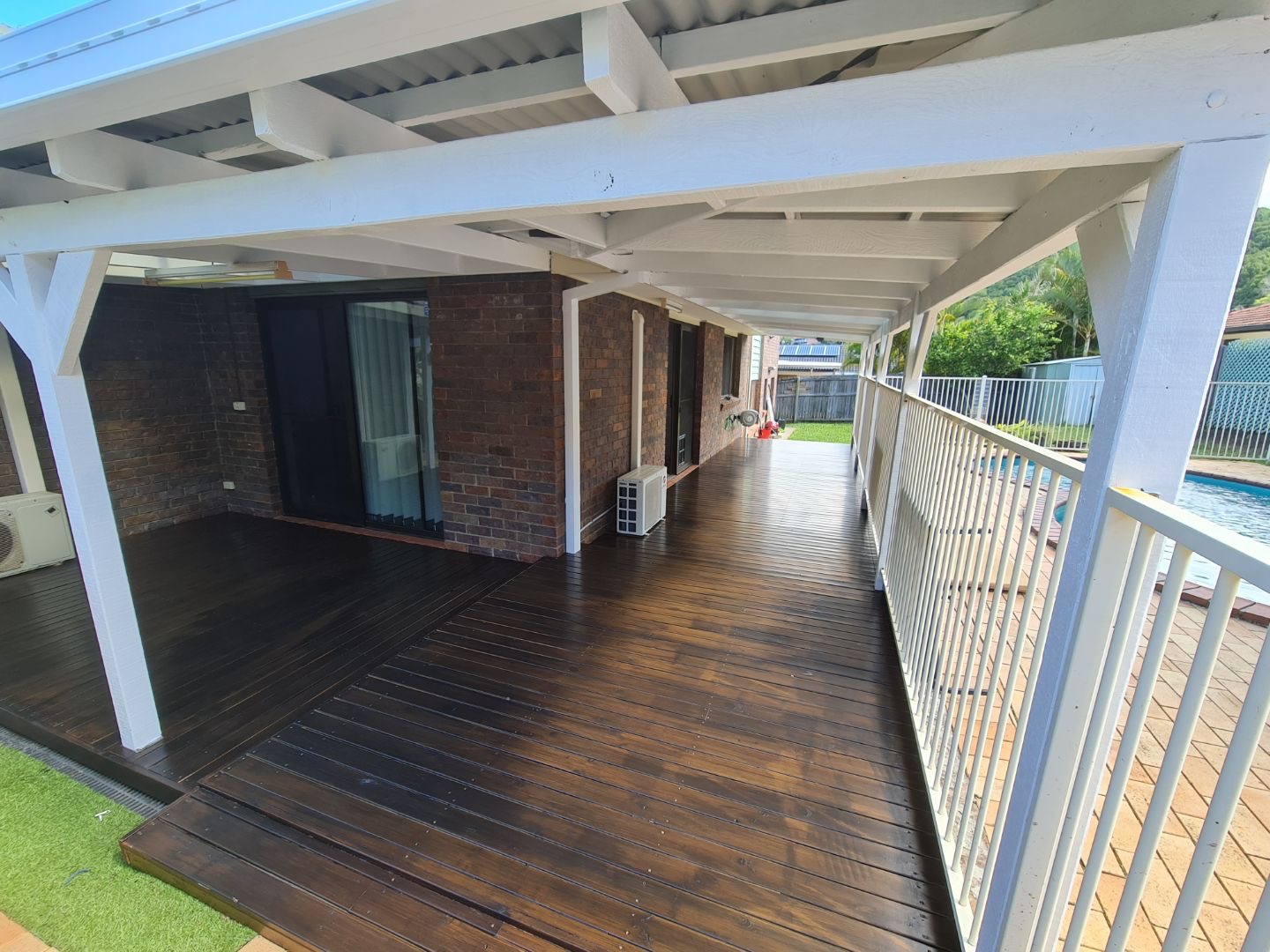 White painted pergola and verandah over a dark timber deck beside a pool